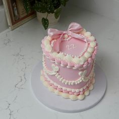 a pink and white cake with a bow on top sitting on a table next to a potted plant