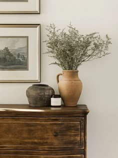 a vase sitting on top of a wooden dresser next to a painting and framed pictures