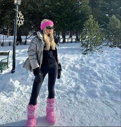 a woman standing in the snow wearing pink boots