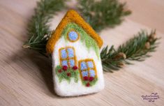 a small felt house ornament on a wooden table next to some pine branches