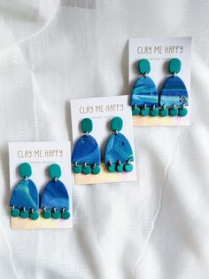 three pieces of blue and green earrings on a white sheet with the words clay me happy