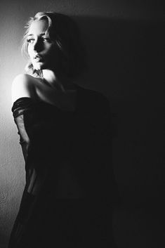 a black and white photo of a woman leaning against a wall with her hand on her hip