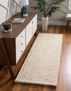 a white rug on top of a wooden floor next to a table with a potted plant