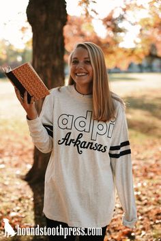 a woman holding up a book in front of a tree