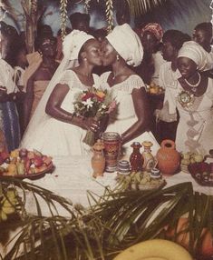 two brides kissing in front of a table full of fruit and other foods on it