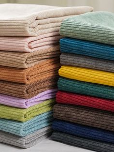 a stack of folded towels sitting on top of a bed next to each other in different colors