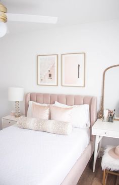 a bed with white sheets and pillows in front of two framed pictures on the wall