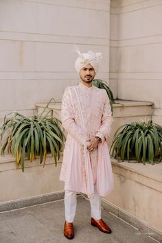 a man standing in front of some plants wearing a pink suit and white turban