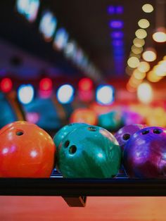 several colorful bowling balls lined up in a row on a rack at a bowling alley