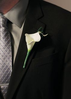 a boutonniere with a white calla lily attached to the lapel of a suit