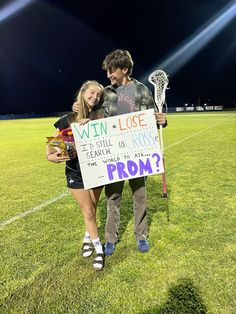 a man and woman standing on top of a soccer field holding a sign that says win lose