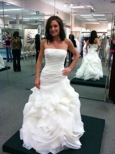 a woman standing in front of a mirror wearing a wedding dress with ruffles