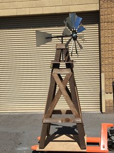 an old fashioned windmill sitting on top of a wooden stand in front of a building