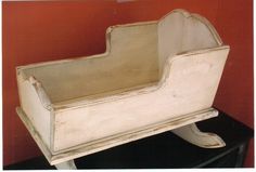 an old white baby crib sitting on top of a black table next to a red wall