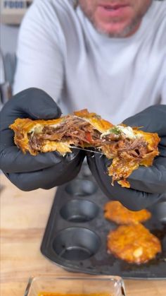 a man in black gloves holding up a piece of food with meat and cheese on it