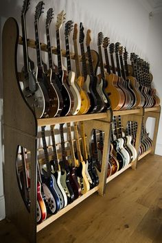 guitars are lined up on wooden shelves in a room