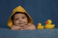 a baby in a bathrobe with two rubber ducks on the side and blue background