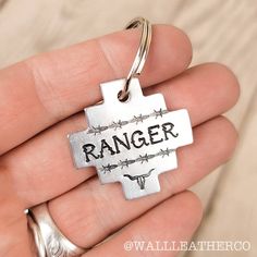 a hand holding a metal keychain with the word ranger on it and barbed wire