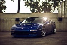 a blue sports car parked in front of a concrete wall with trees on the other side