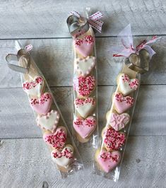 three heart shaped cookies in cellophane wrappers on a wooden table with ribbon