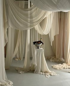 a room with white draping and flowers on the table in front of it