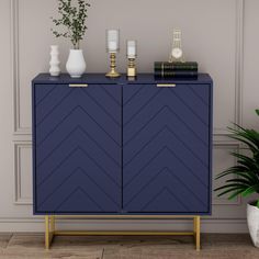 a blue cabinet with gold handles and two candles on it next to a potted plant