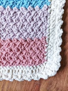 a crocheted dishcloth is laying on a wooden surface with the colors of blue, pink, and white