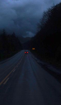 an empty road at night with the lights on and dark clouds in the sky above