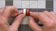 two hands are working on an orange and white piece of fabric with thread attached to it