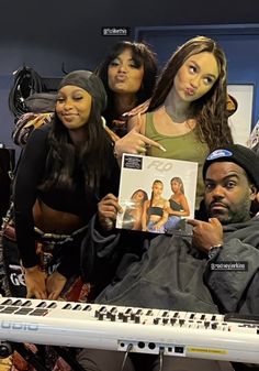 four people are posing for a photo while holding up a record and an electronic keyboard