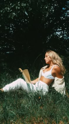 a woman is sitting in the grass with her legs crossed and holding a book while looking off into the distance