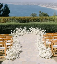 an outdoor ceremony setup with white flowers and wooden chairs on the walkway to the beach