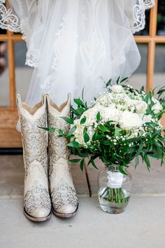 a bouquet of white flowers and cowboy boots are sitting on the ground next to a window