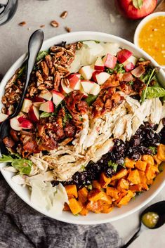 a white bowl filled with chicken, apples and cranberry salad next to orange sauce