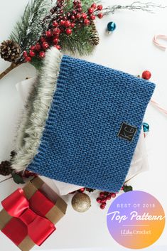 a blue knitted blanket next to christmas decorations and presents on a white table with red ribbon