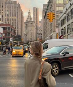 a woman is walking across the street with her back turned to the camera as cars drive by