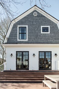 a white house with two large windows and steps leading to the front door, on a sunny day