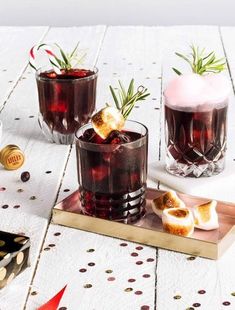 three glasses filled with drinks sitting on top of a wooden table next to candy canes