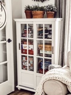 a living room with a white bookcase and potted plants on the top shelf