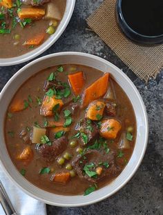 two bowls of beef stew with carrots, peas and parsley on the side