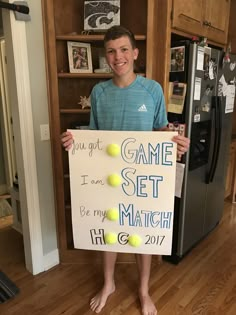 a young boy holding up a sign that says game set match with tennis balls on it