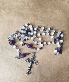 This is a gorgeous five-decade Catholic rosary. These pieces were made using gunmetal and silver findings, centers, and crucifixes. The decade beads are 6mm ivory cat eye glass beads. The Father beads are 8mm chevron amethyst. The rosary chain is hand wired using gunmetal eye pins. This is handmade chain, not store-bought. The sections are connected with small bits of gunmetal chain. The jump rings, centers, and crucifixes are dark silver color. They go well with the gunmetal chain. The center i Silver Rosary With Natural Stones For Gift, Silver Rosary With Natural Stones As A Gift, Silver Spiritual Rosary For Healing, Handmade Silver Rosary For Healing, Chakra Colors, Heart Of Jesus, Rosary Chain, Eye Pins, Rosary Catholic