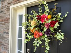 a wreath made out of flowers hangs on the front door's black door frame