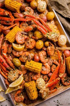 lobster, corn on the cob and potatoes with lemon wedges in a pan