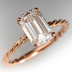 an emerald - cut diamond sits in the center of a rose gold engagement ring with twisted band