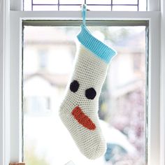 a crocheted stocking hanging from a window sill with a snowman face on it