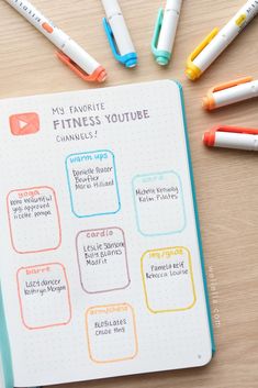 an open planner with markers and pens on the table next to it is a notebook full of fitness trackers