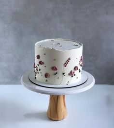 a white cake with red flowers on it sitting on top of a wooden stand in front of a gray wall