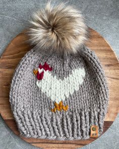 a gray knitted hat with white and red birds on it, sitting on top of a wooden board