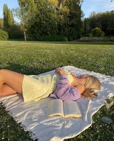 a woman laying on a blanket reading a book